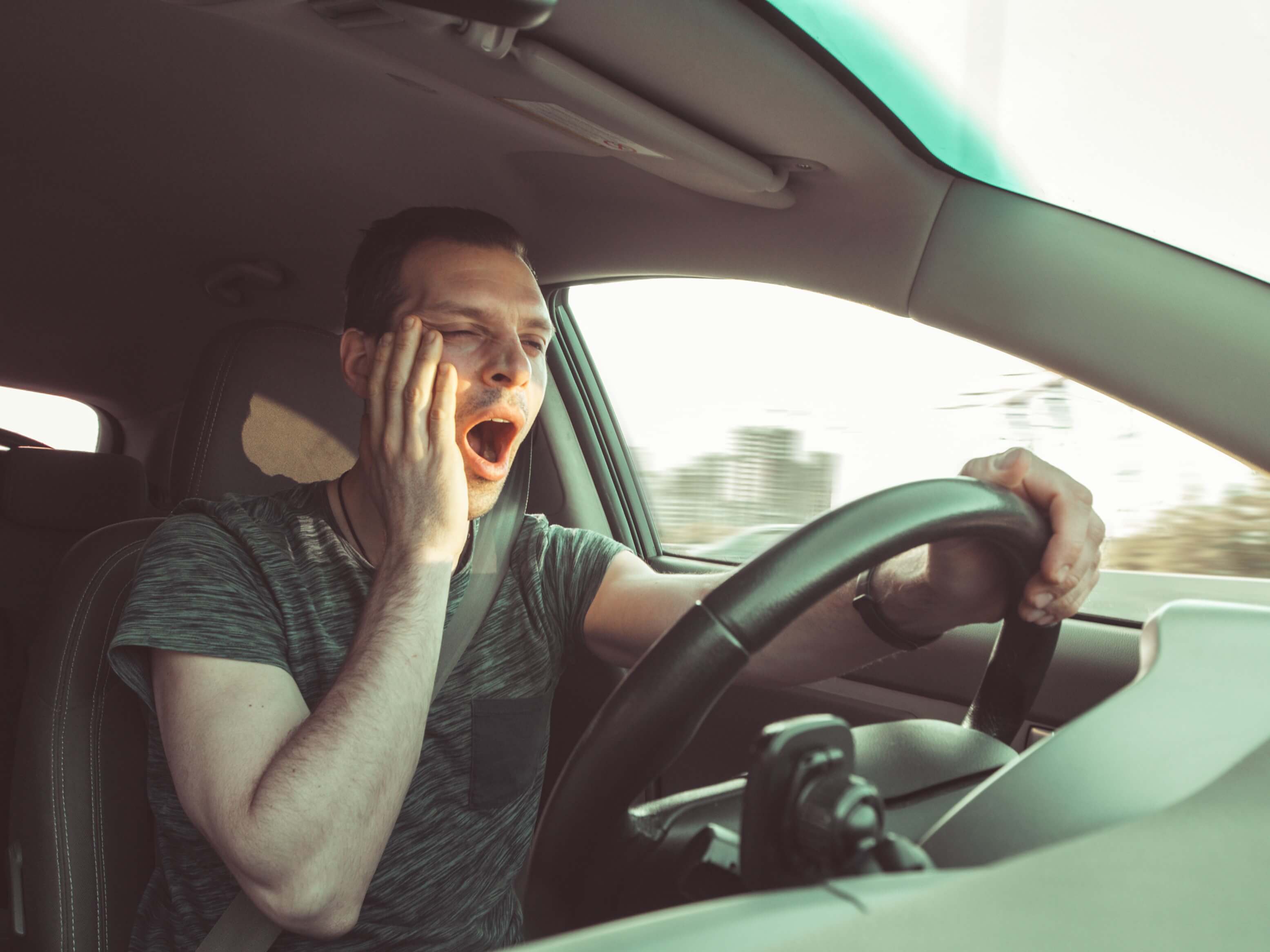 自動車の運転席で欠伸をする男性